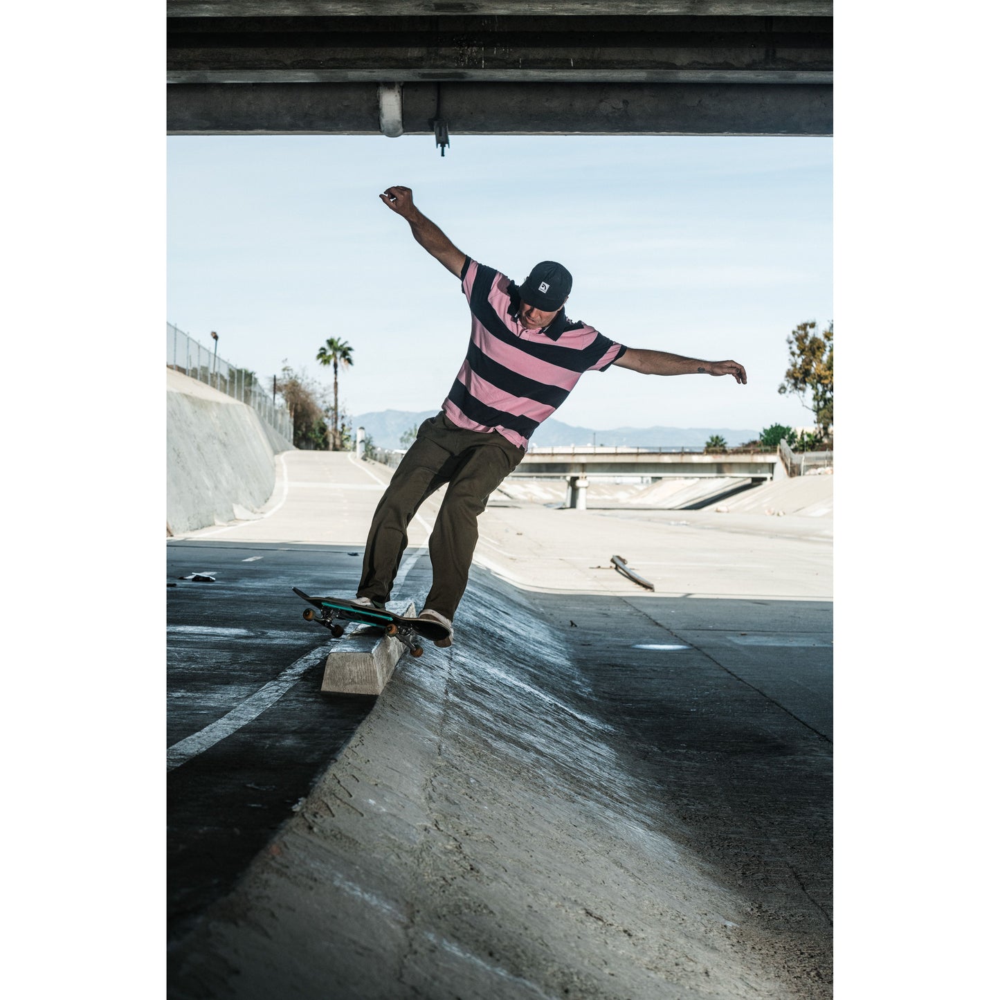 Skateboarder wearing baggy skate pants performing a trick on a concrete surface with a clear sky in the background.