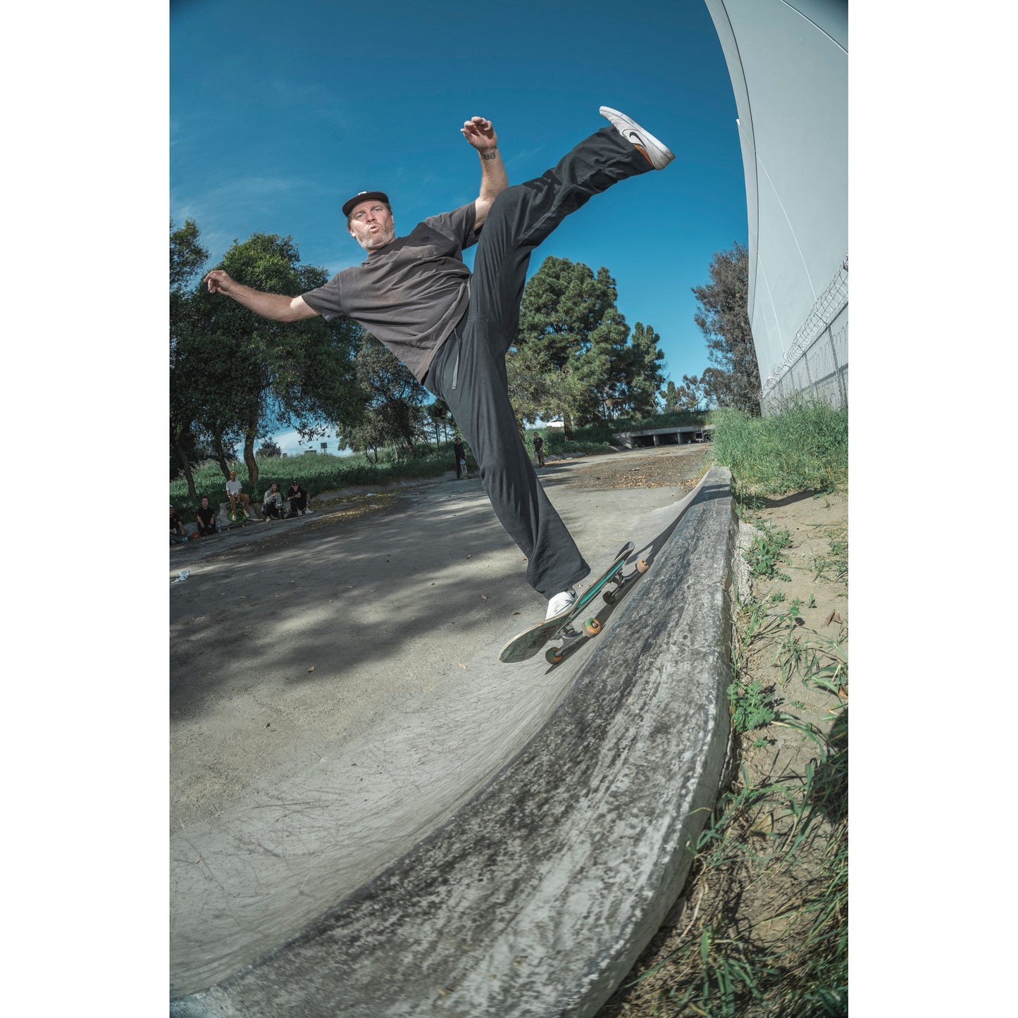 Kyle Leeper skateboarding on a concrete ledge with trees and a clear sky in the background wearing limpies black baggy skate pants