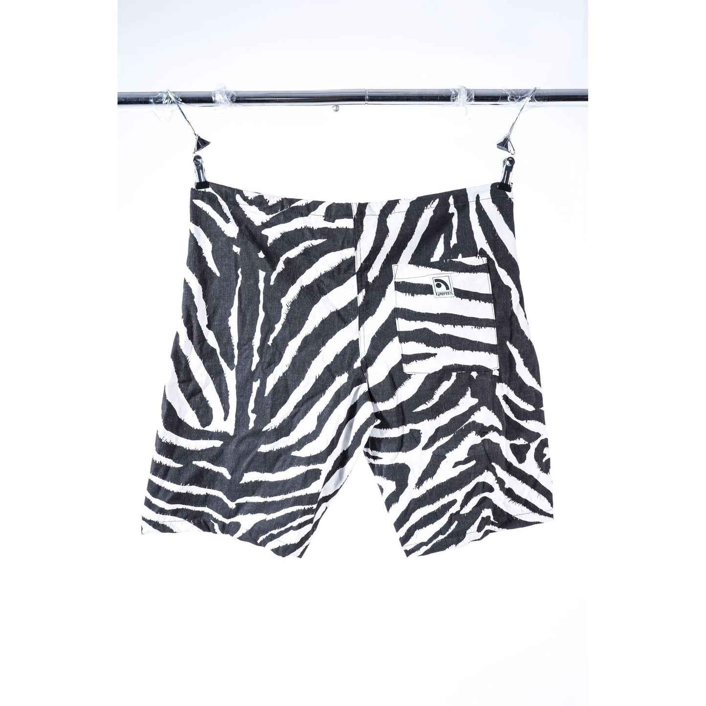 Black and white zebra print baggy skate shorts hanging from a metal clothesline against a white background.
