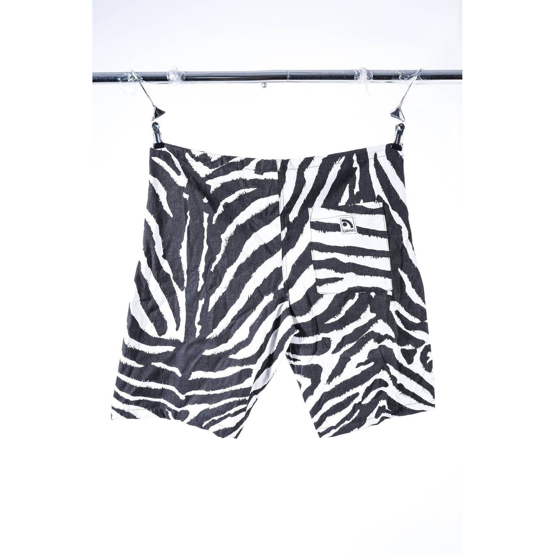 Black and white zebra print baggy skate shorts hanging from a metal clothesline against a white background.