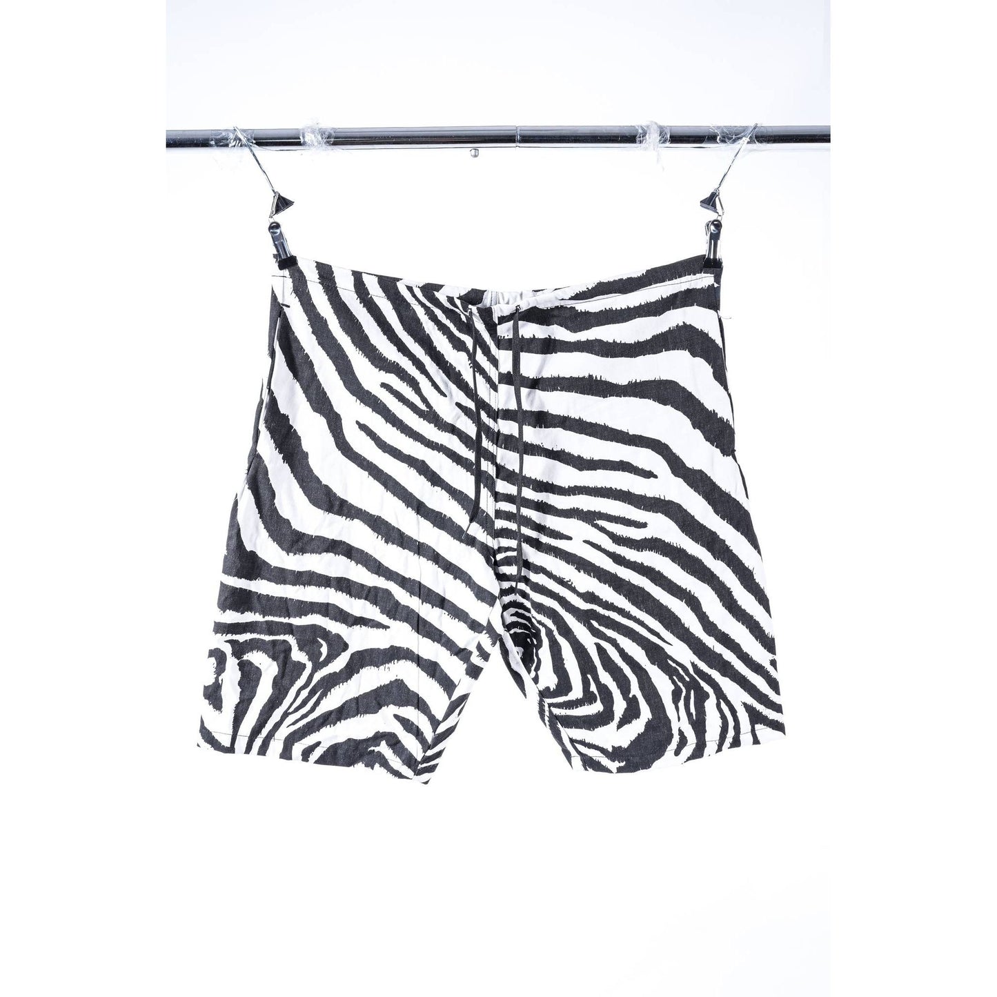 Zebra-print baggy skate shorts with a black and white pattern, hanging from clips on a metal clothing rack against a white background.