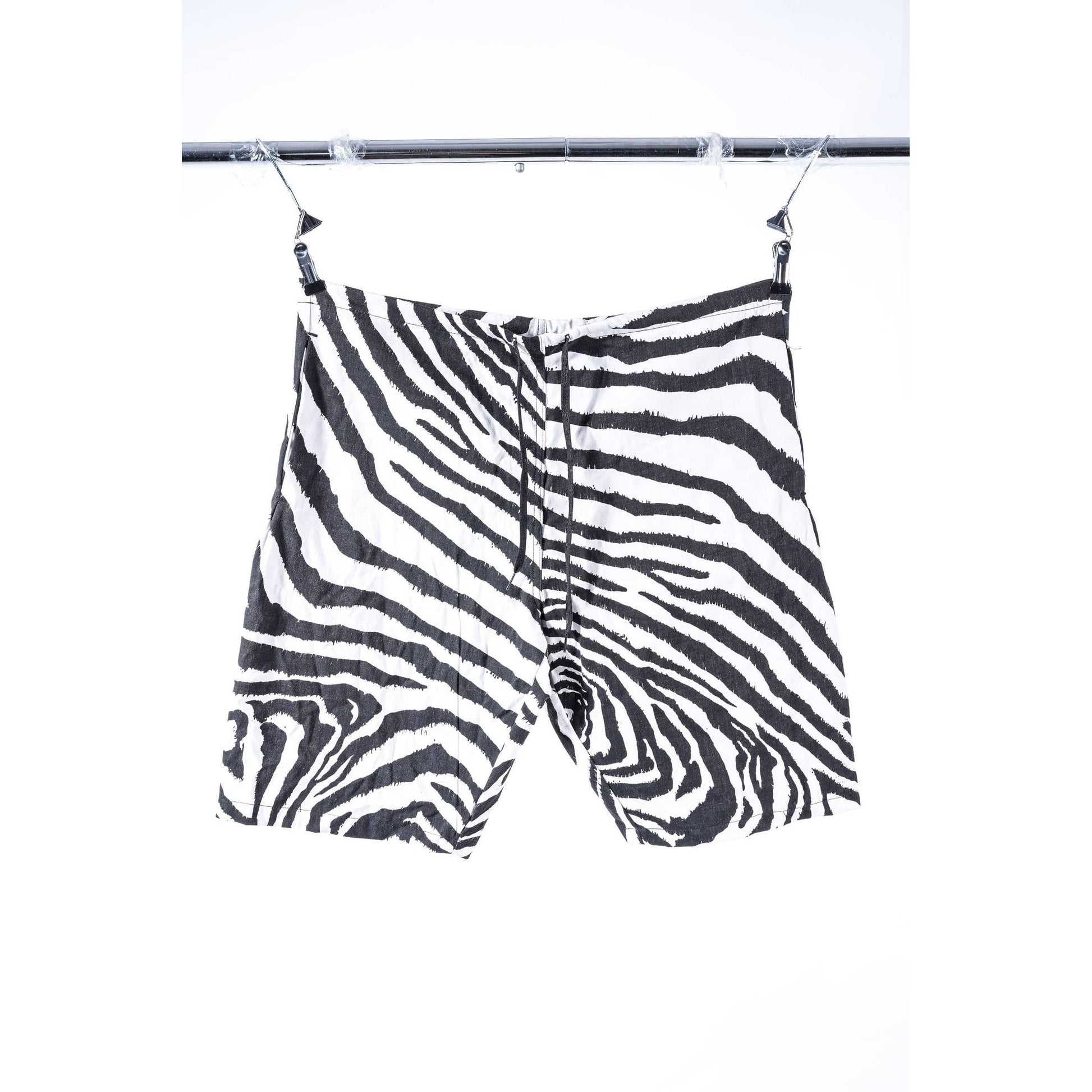 Zebra-print baggy skate shorts with a black and white pattern, hanging from clips on a metal clothing rack against a white background.