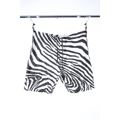 Zebra-print baggy skate shorts with a black and white pattern, hanging from clips on a metal clothing rack against a white background.