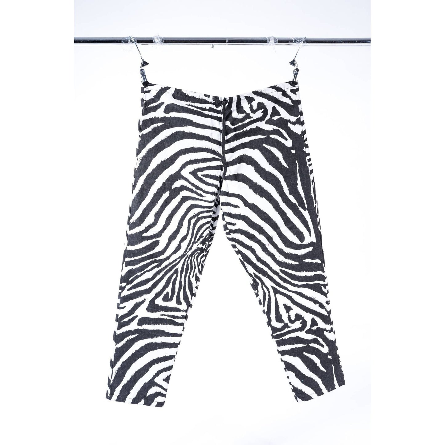 Black and white zebra print cropped baggy skate pants hanging from clips on a metal rail against a white background.