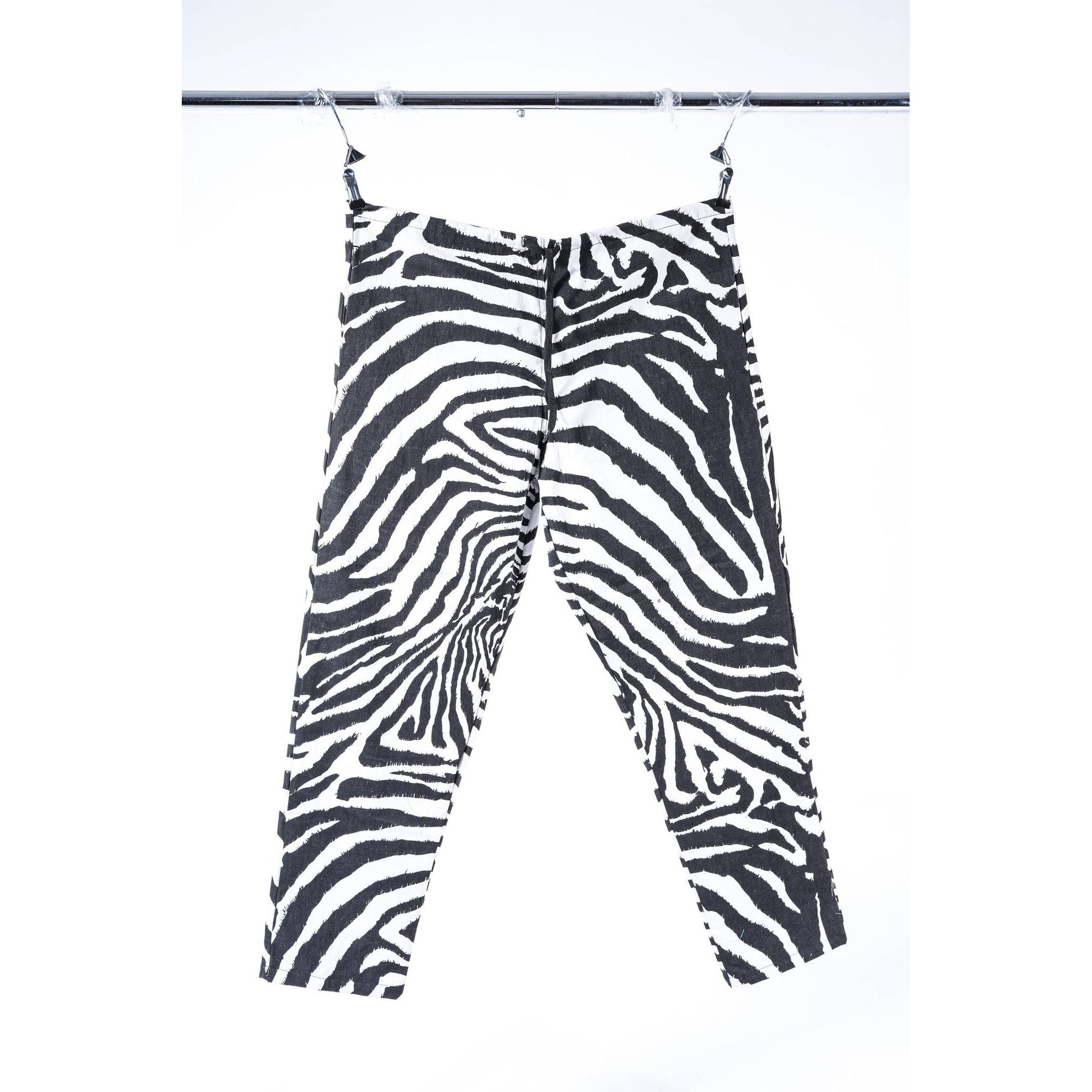 Black and white zebra print cropped baggy skate pants hanging from clips on a metal rail against a white background.