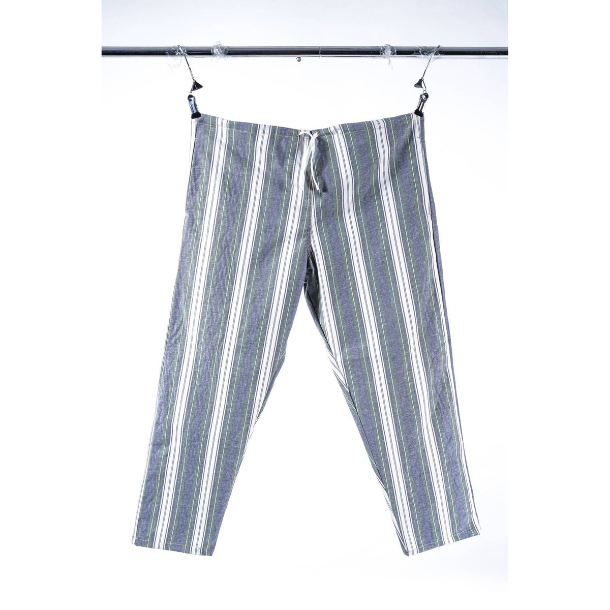 A pair of cropped pants with vertical stripes in gray, white, and muted blue, hanging from a black metal clothesline against a white background.