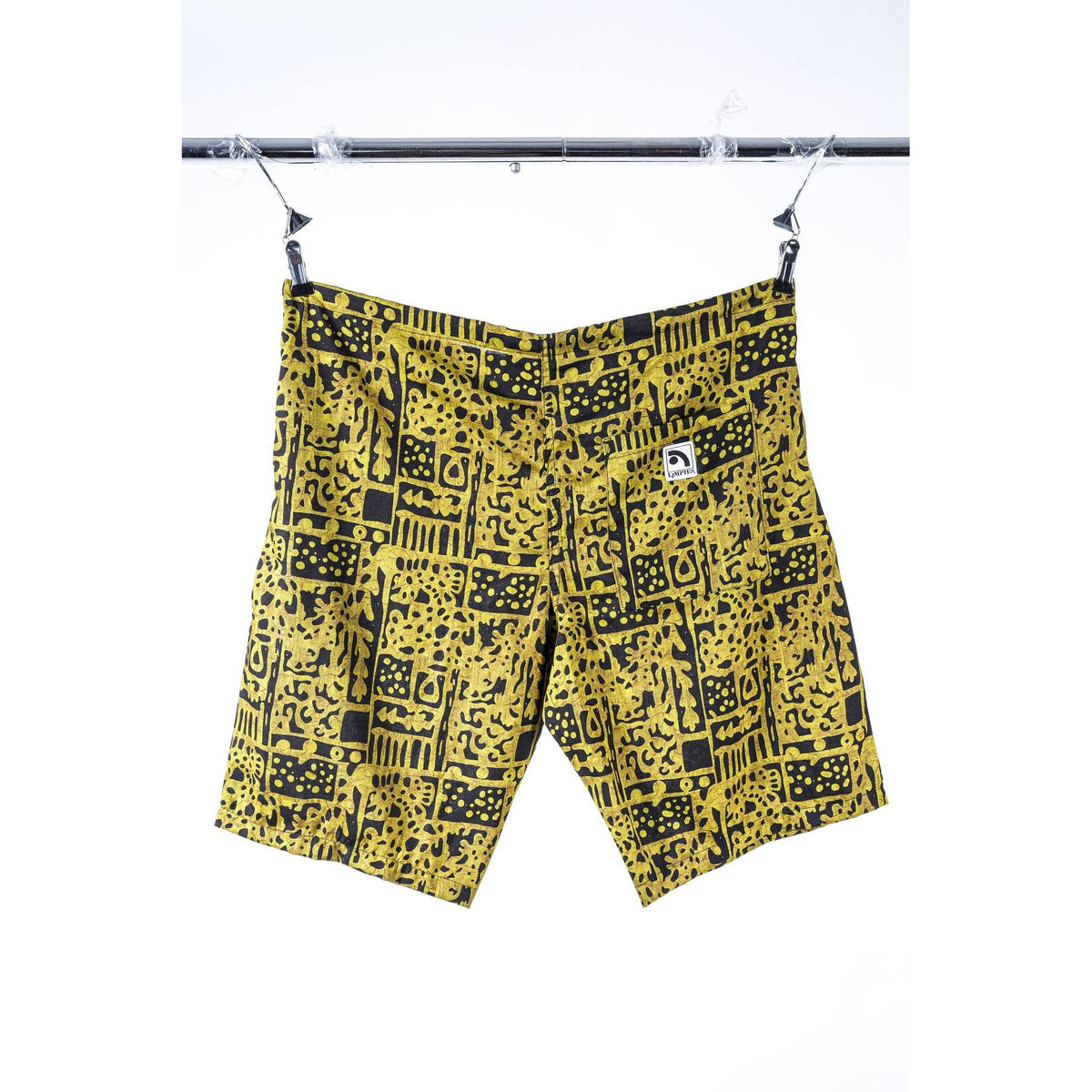 Yellow and black patterned Limpies baggy skate shorts hanging from a metal bar with clips against a white background. A small white square logo patch is visible on the left hip.