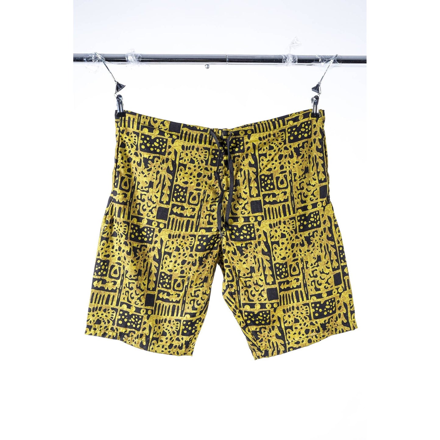 Yellow and black patterned  Limpies baggy skate shorts hanging from a black metal clothesline against a white background.