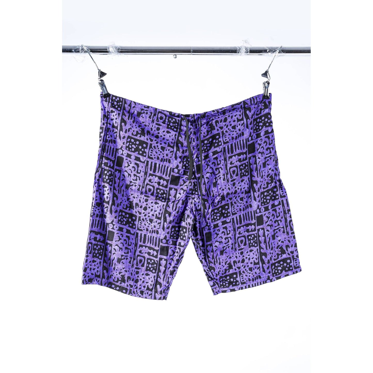 Purple and black patterned Limpies baggy skate shorts hanging from clips on a metal bar against a white background.