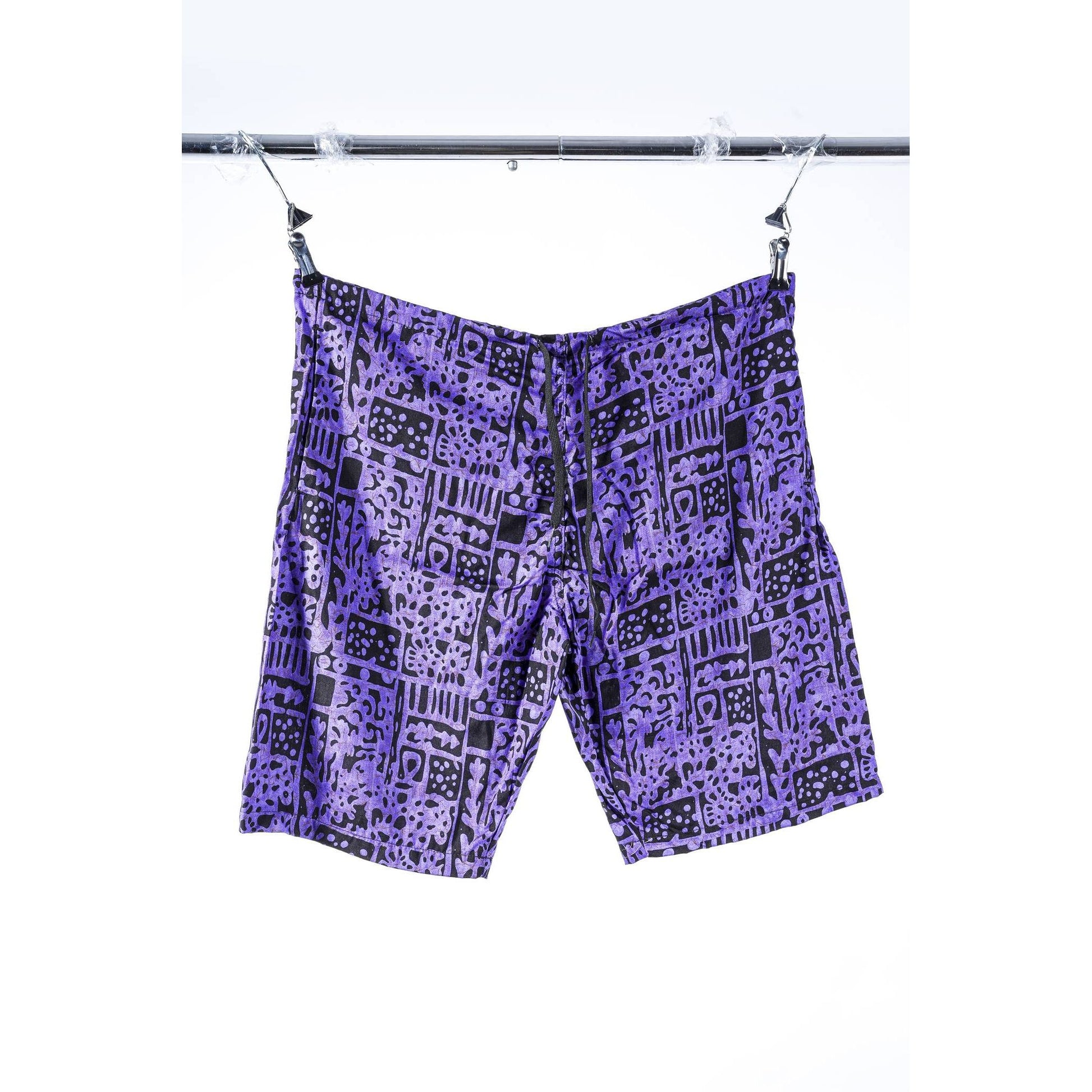 Purple and black patterned Limpies baggy skate shorts hanging from clips on a metal bar against a white background.
