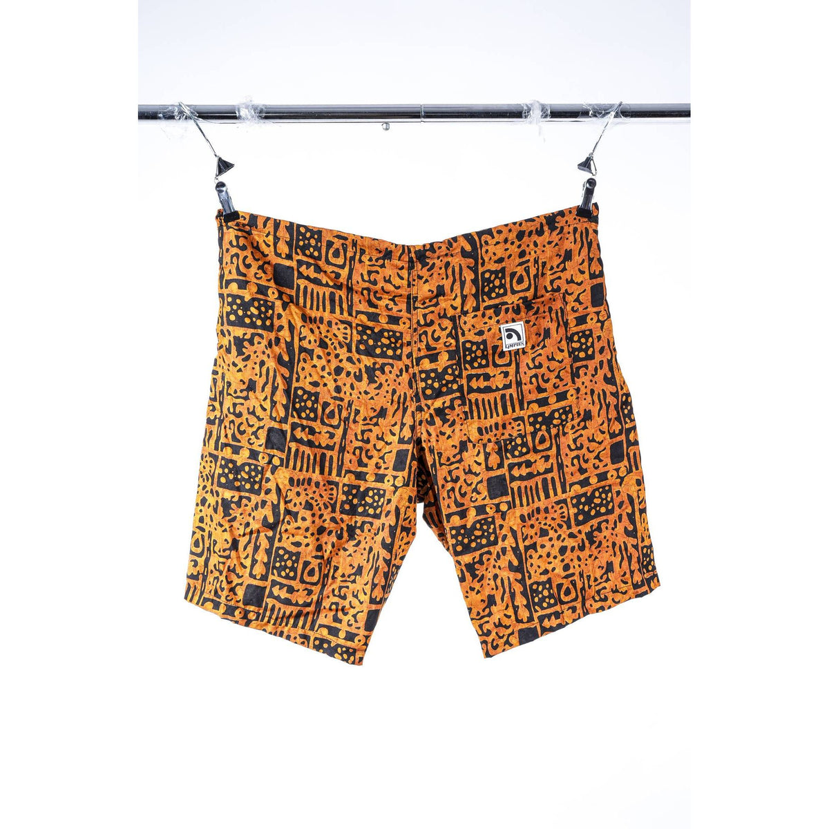 Orange and black patterned Limpies baggy skate shorts hanging from clips on a metal rack against a white background. A small white square logo patch is visible on the upper right hip.