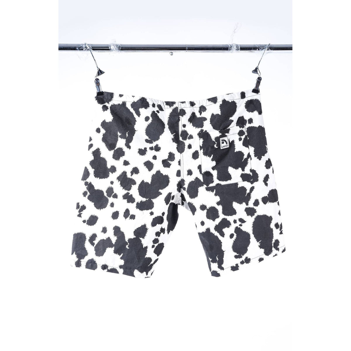 Black and white cow print Limpies baggy skate shorts hanging from a metal hanger bar against a white background.
