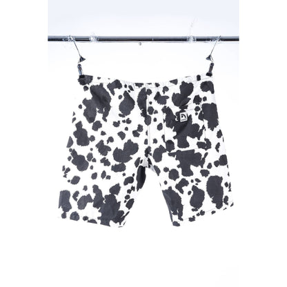 Black and white cow print Limpies baggy skate shorts hanging from a metal hanger bar against a white background.