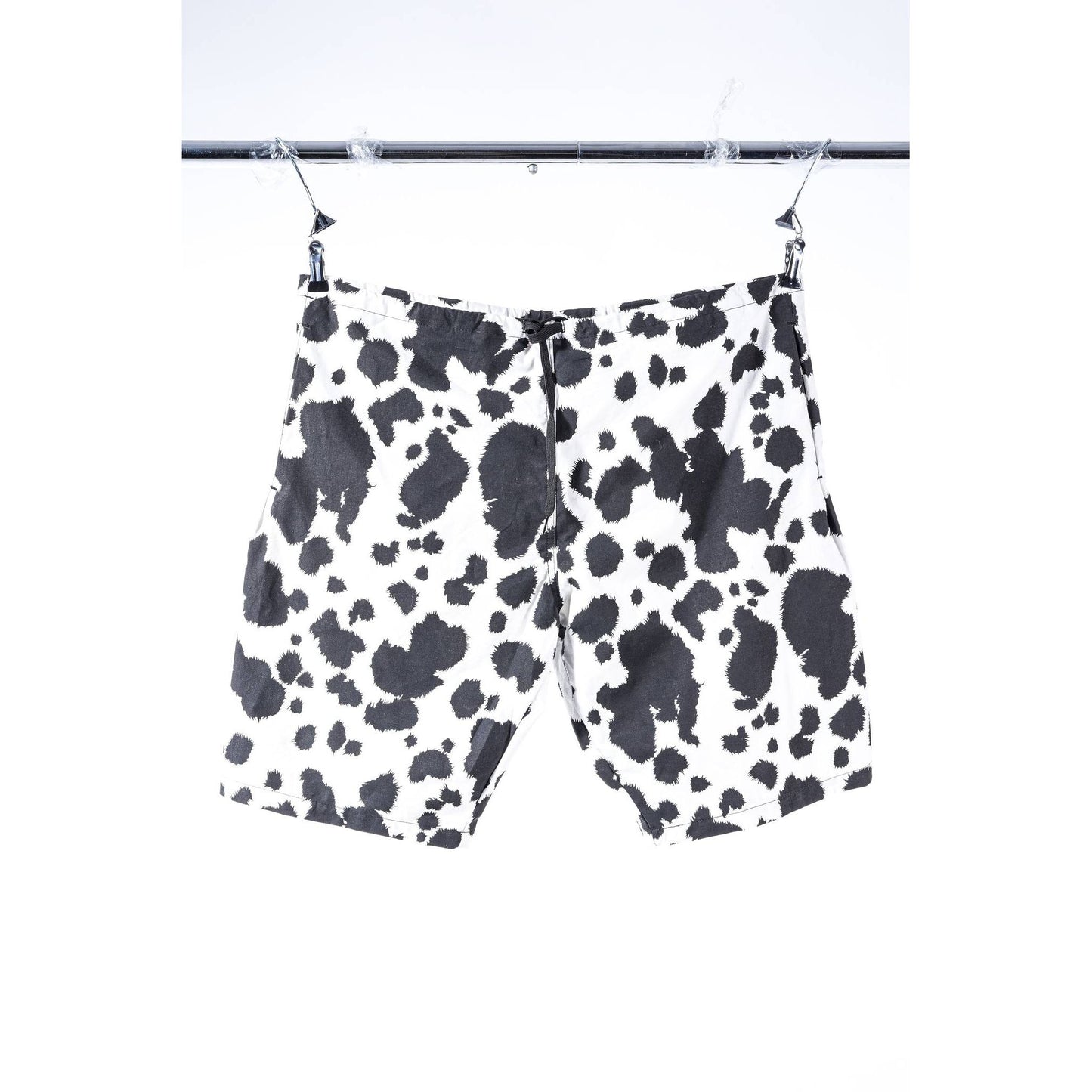 Black and white cow print Limpies baggy skate shorts hanging from a metal hanger on a clothing rack against a white background.