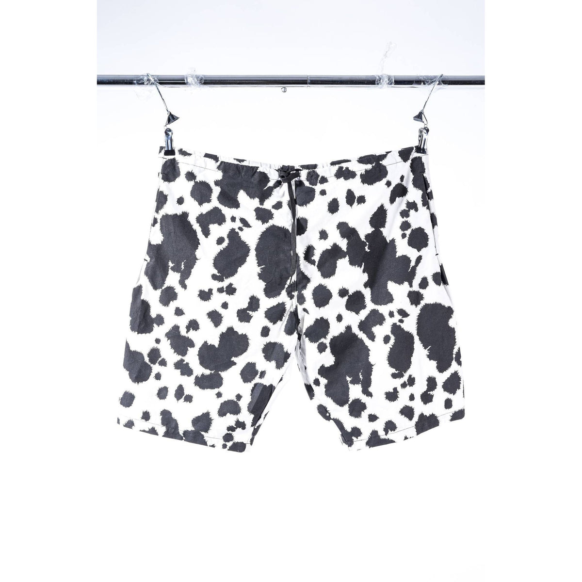 Black and white cow print Limpies baggy skate shorts hanging from a metal hanger on a clothing rack against a white background.