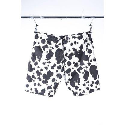Black and white cow print Limpies baggy skate shorts hanging from a metal hanger on a clothing rack against a white background.