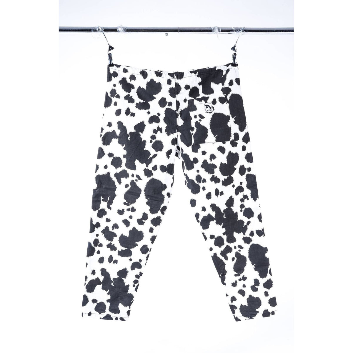 Black and white cow print Limpies baggy skate pants hanging from a metal hanger against a white background.