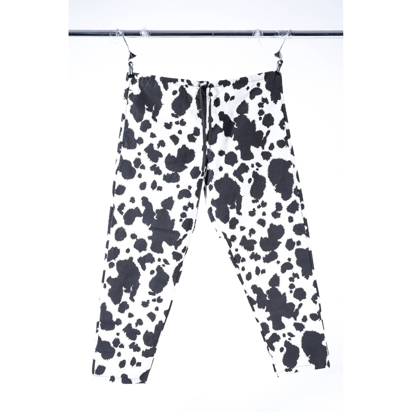 Black and white cow print Limpies baggy skate pants hanging from clips on a metal rail against a white background.