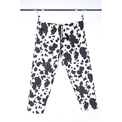 Black and white cow print Limpies baggy skate pants hanging from clips on a metal rail against a white background.