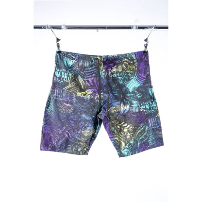 A pair of men's Limpies baggy skate shorts featuring an abstract, metallic-looking pattern in purple, teal, and gold, hanging from clips on a metal rack against a white background.
