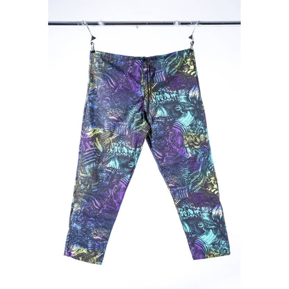 A pair of cropped Limpies baggy skate pants with an abstract, multicolored pattern featuring purple, teal, blue, and gold, hanging from clips on a black clothing rack against a white background.