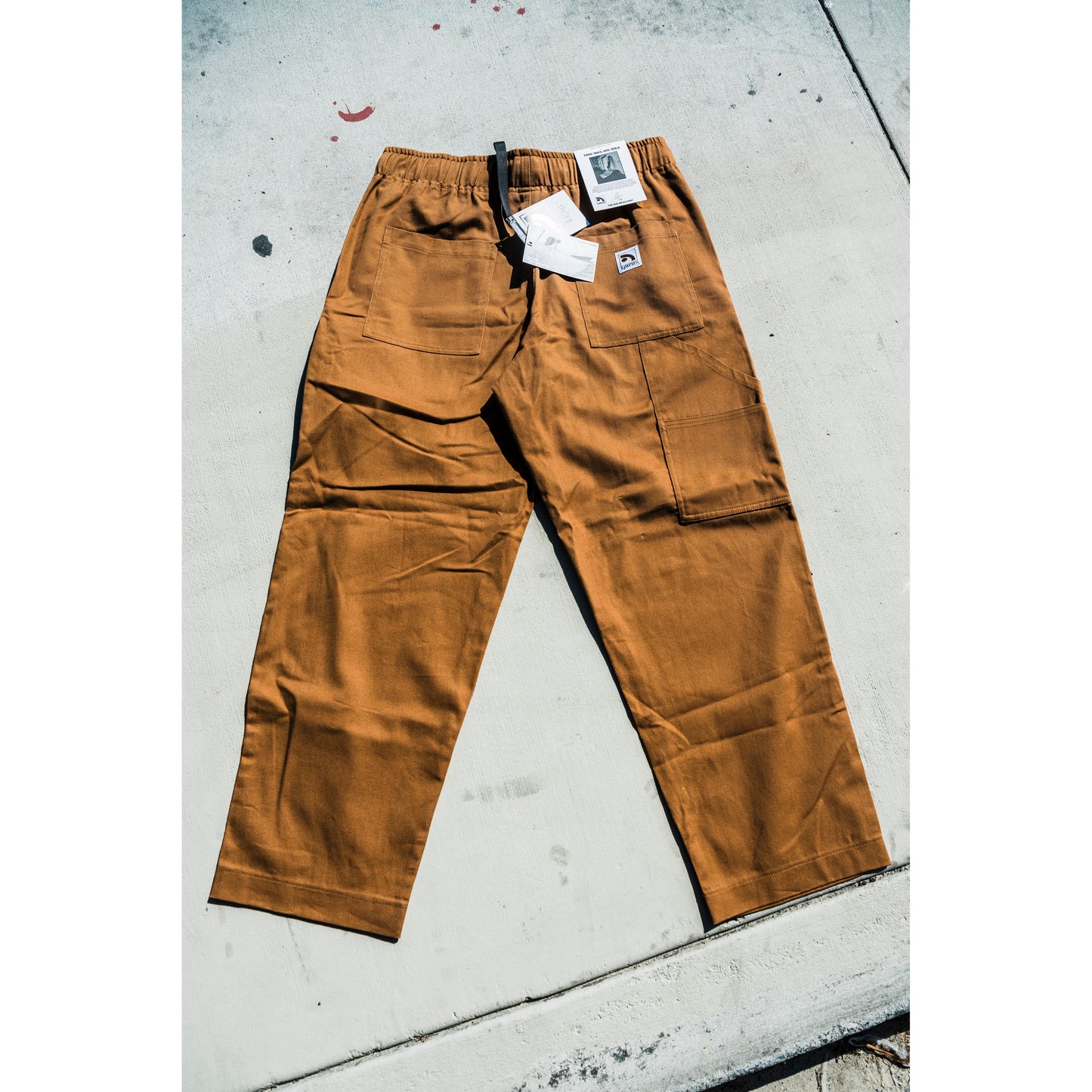 Brown baggy skate pants with tags on a concrete surface