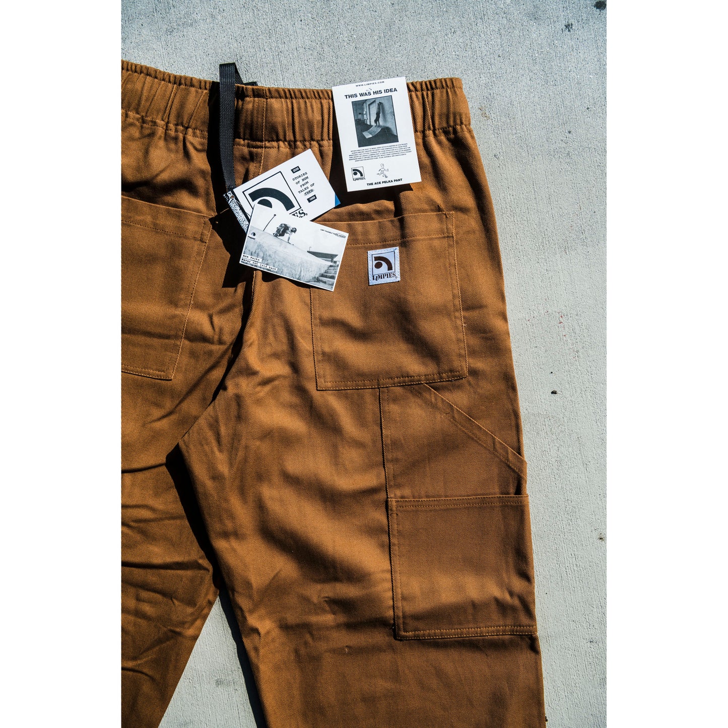 Brown baggy skate pants with tags on a gray concrete surface
