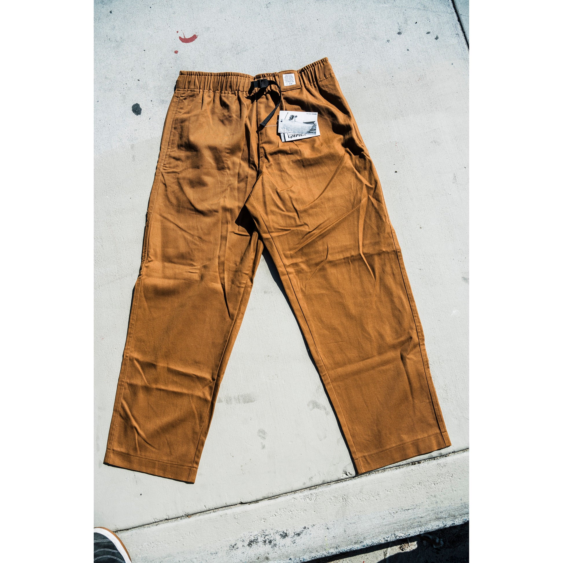 Brown baggy skate pants with a tag on a concrete surface