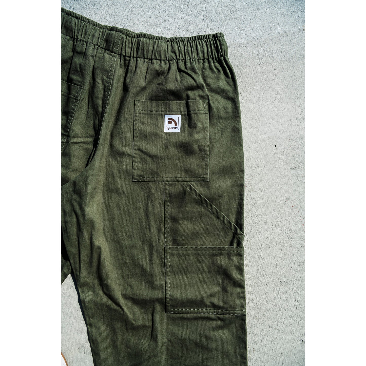 olive green baggy skate pants with a logo on a gray surface