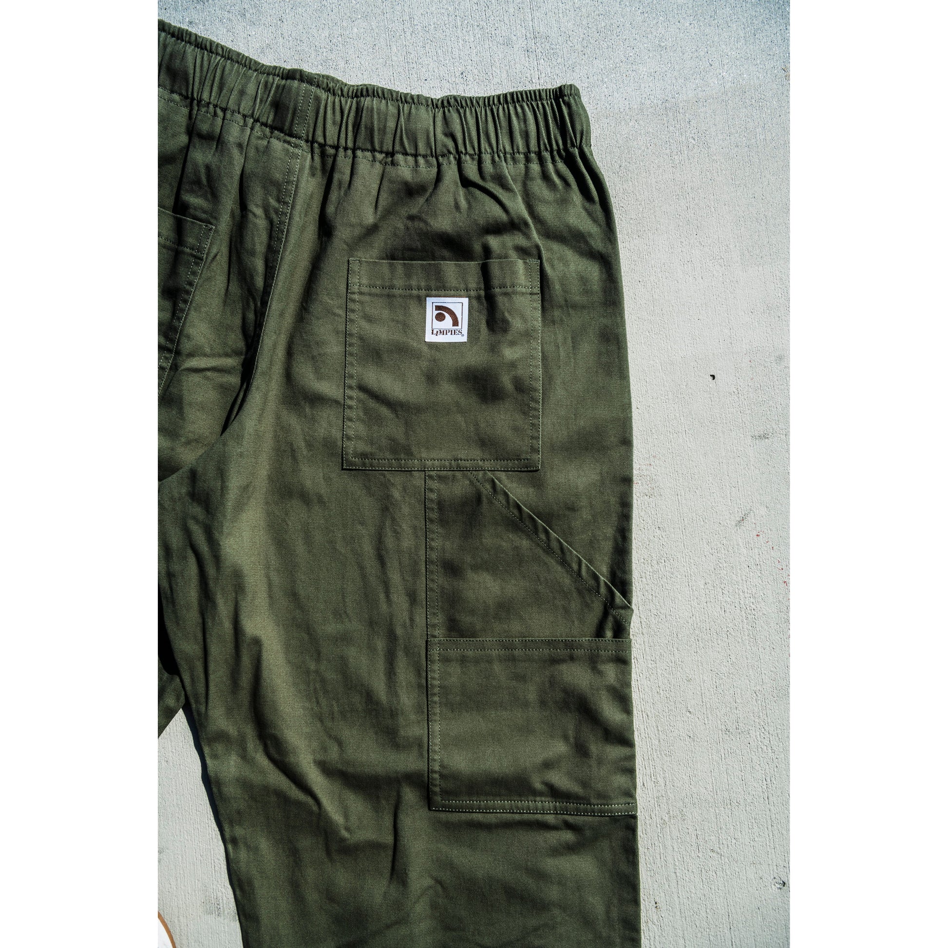 olive green baggy skate pants with a logo on a gray surface