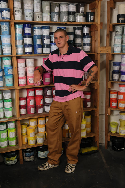Man wearing baggy skate pants standing in front of shelves filled with various containers in a storage room.