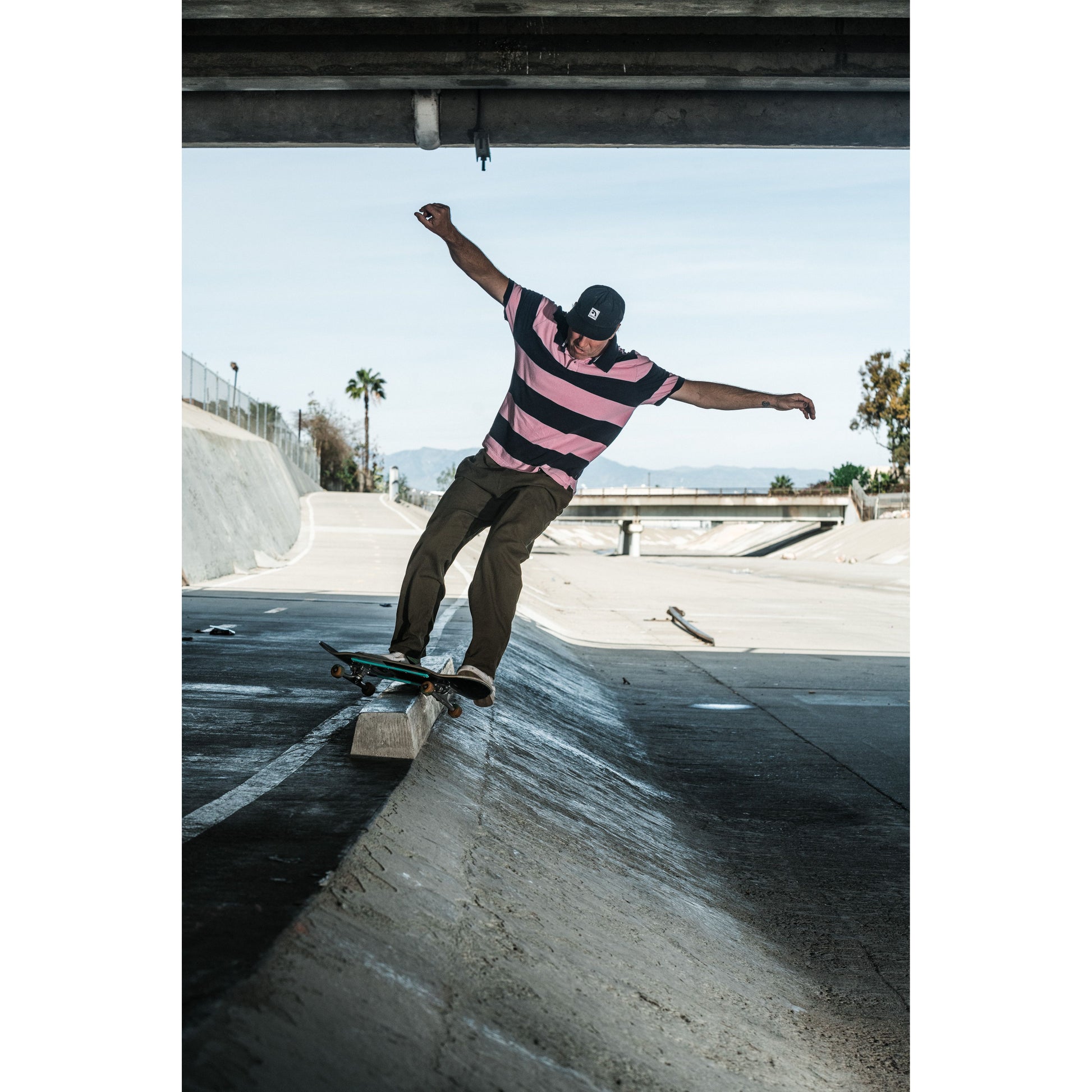 Skateboarder wearing baggy skate pants performing a trick on a concrete surface with a clear sky in the background.