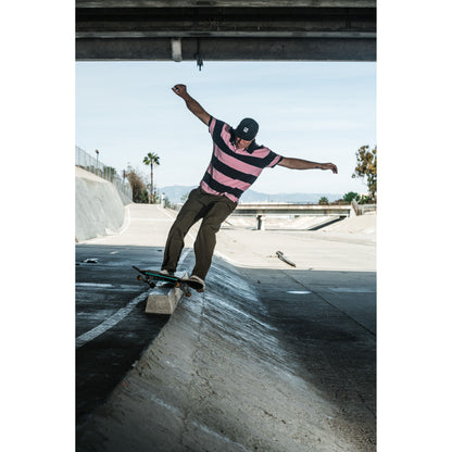 Skateboarder wearing baggy skate pants performing a trick on a concrete surface with a clear sky in the background.