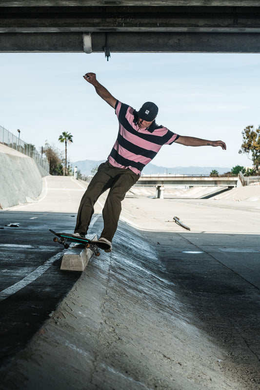 Skateboarder wearing baggy skate pants performing a trick on a concrete surface with a clear sky in the background.