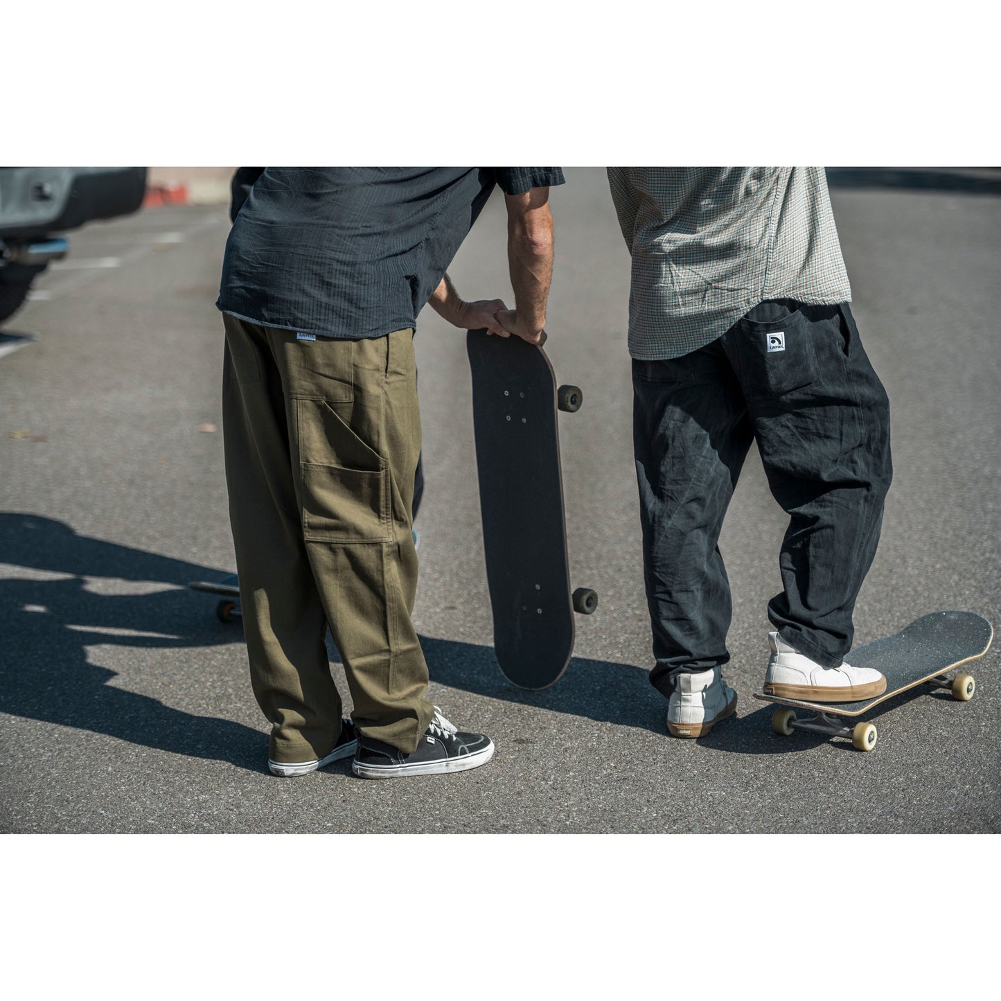 Two people standing on a street with skateboards, wearing baggy skate clothing.