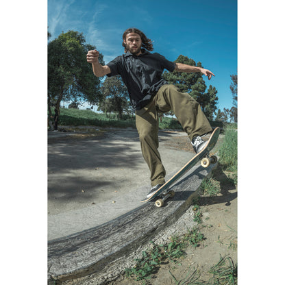 Person skateboarding in baggy skate pants on a concrete ledge with trees and blue sky in the background