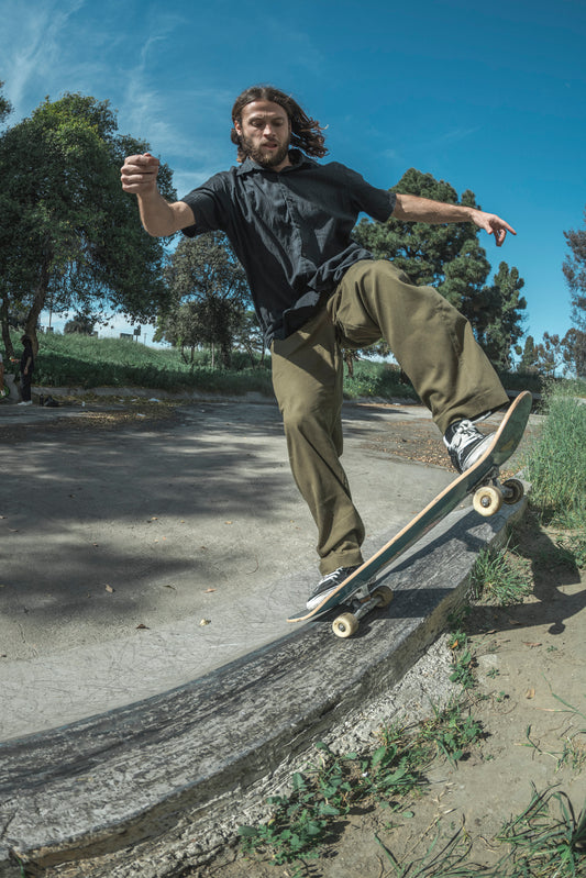 Person skateboarding in baggy skate pants on a concrete ledge with trees and blue sky in the background