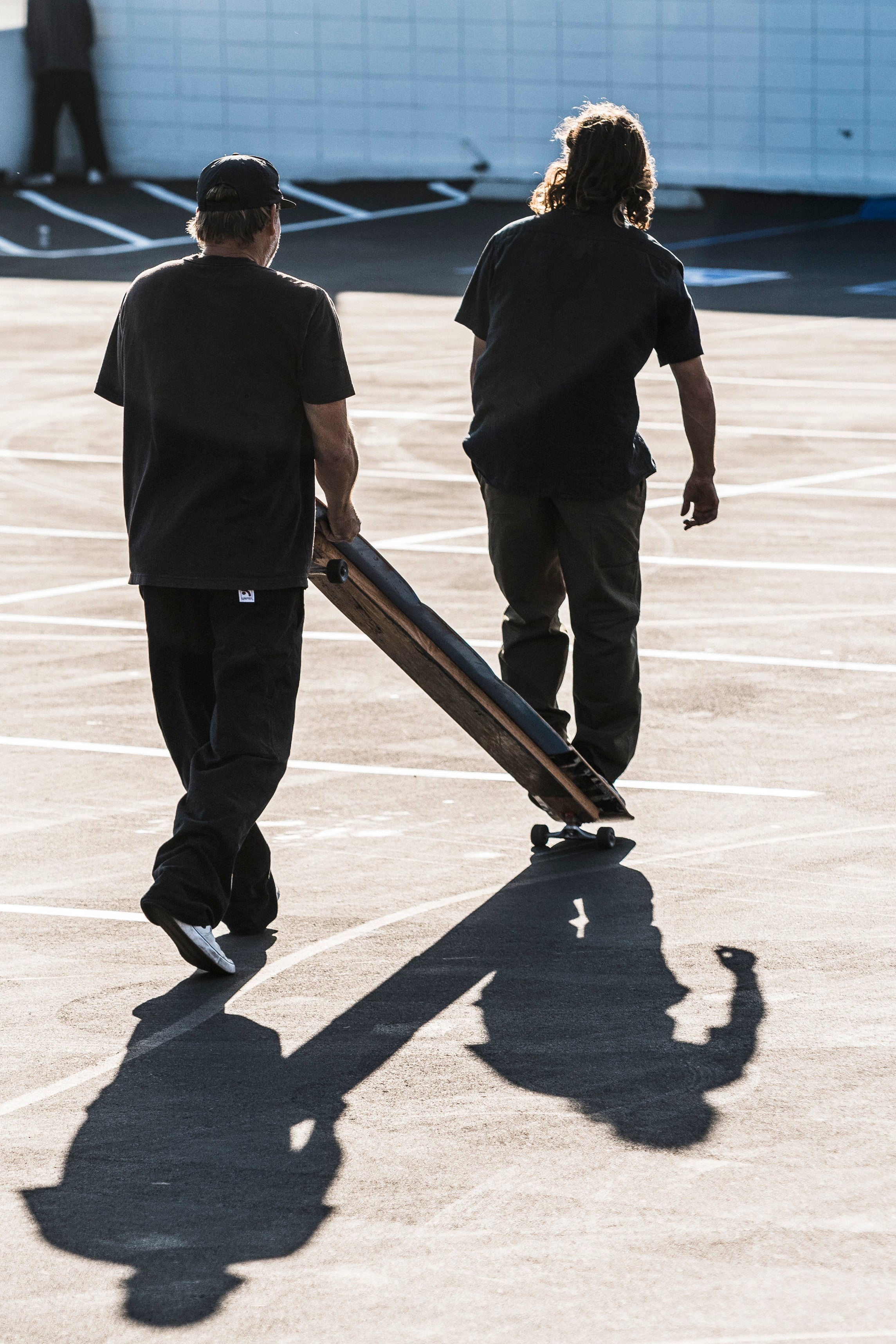 Two people walking with a skateboard on a concrete surface