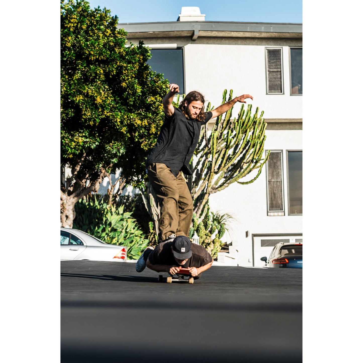 Person skateboarding in baggy skate pants on a residential street with a house and cactus in the background