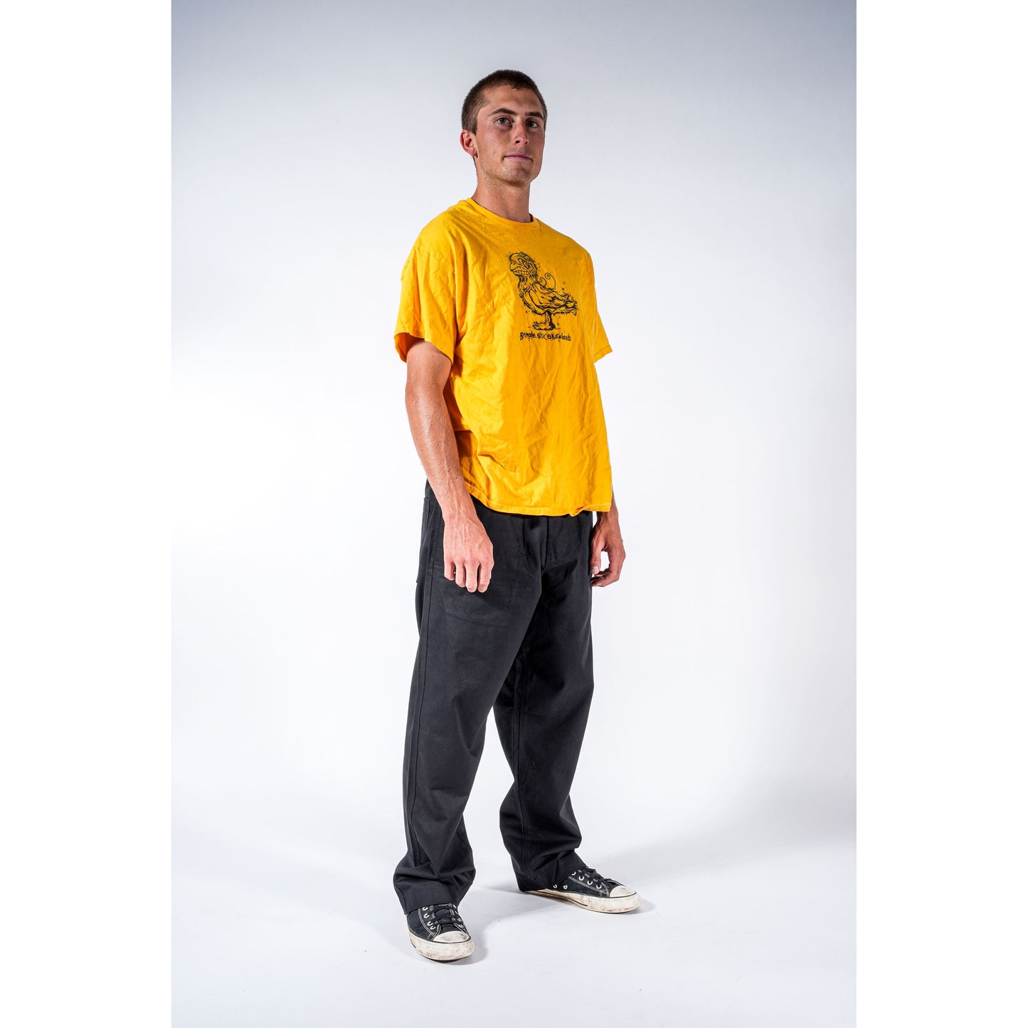 A man modeling. He is wearing loose black baggy skate pants and black sneakers with white soles, standing against a light gray studio background.