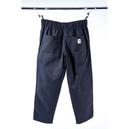 Black baggy skate pants with an elastic waistband, two large patch pockets, and a small white brand tag on the back pocket, hanging from clips on a metal bar against a white background.