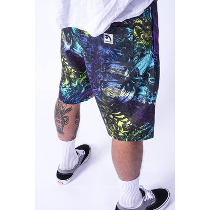 A person wearing colorful abstract-print Limpies baggy skate shorts with a small white logo patch, styled with a white t-shirt, white socks, and black sneakers against a white studio background.