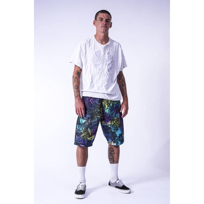A man modeling a white t-shirt and colorful patterned Limpies baggy skate shorts against a light gray studio background.