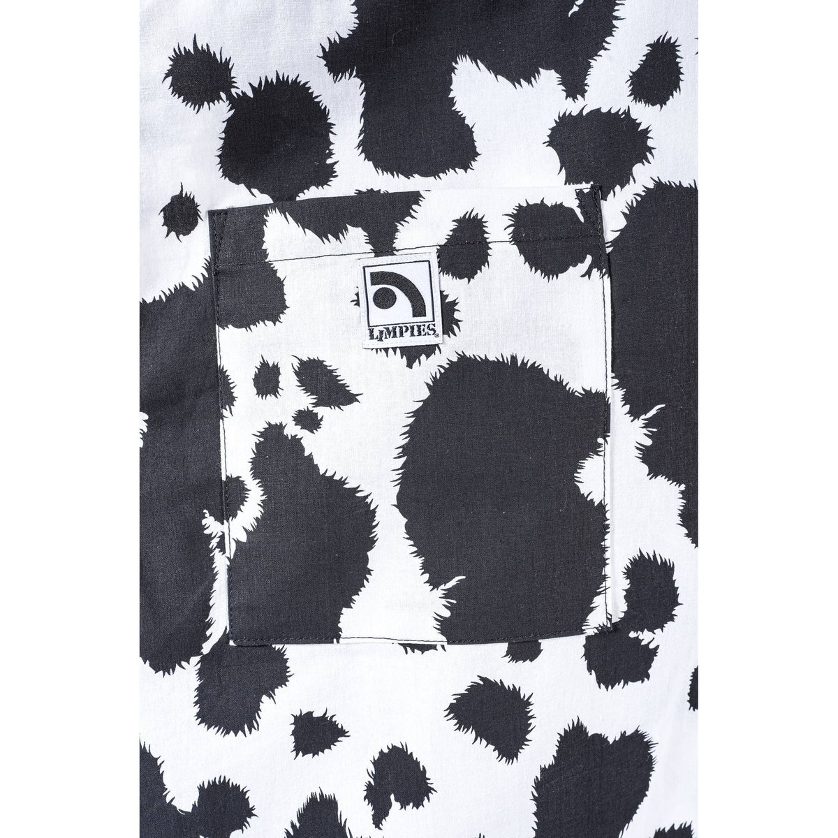 Close-up of a black and white cow print  Limpies baggy skate pants fabric with a front pocket featuring a visible Limpies Brand label.