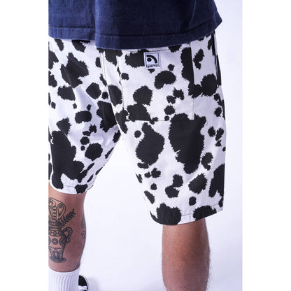 A close-up of a person wearing white  Limpies baggy skate shorts with a bold black cow-print pattern, paired with a dark navy t-shirt. The brand tag on the back pocket reads 'LIFEFILTER'.