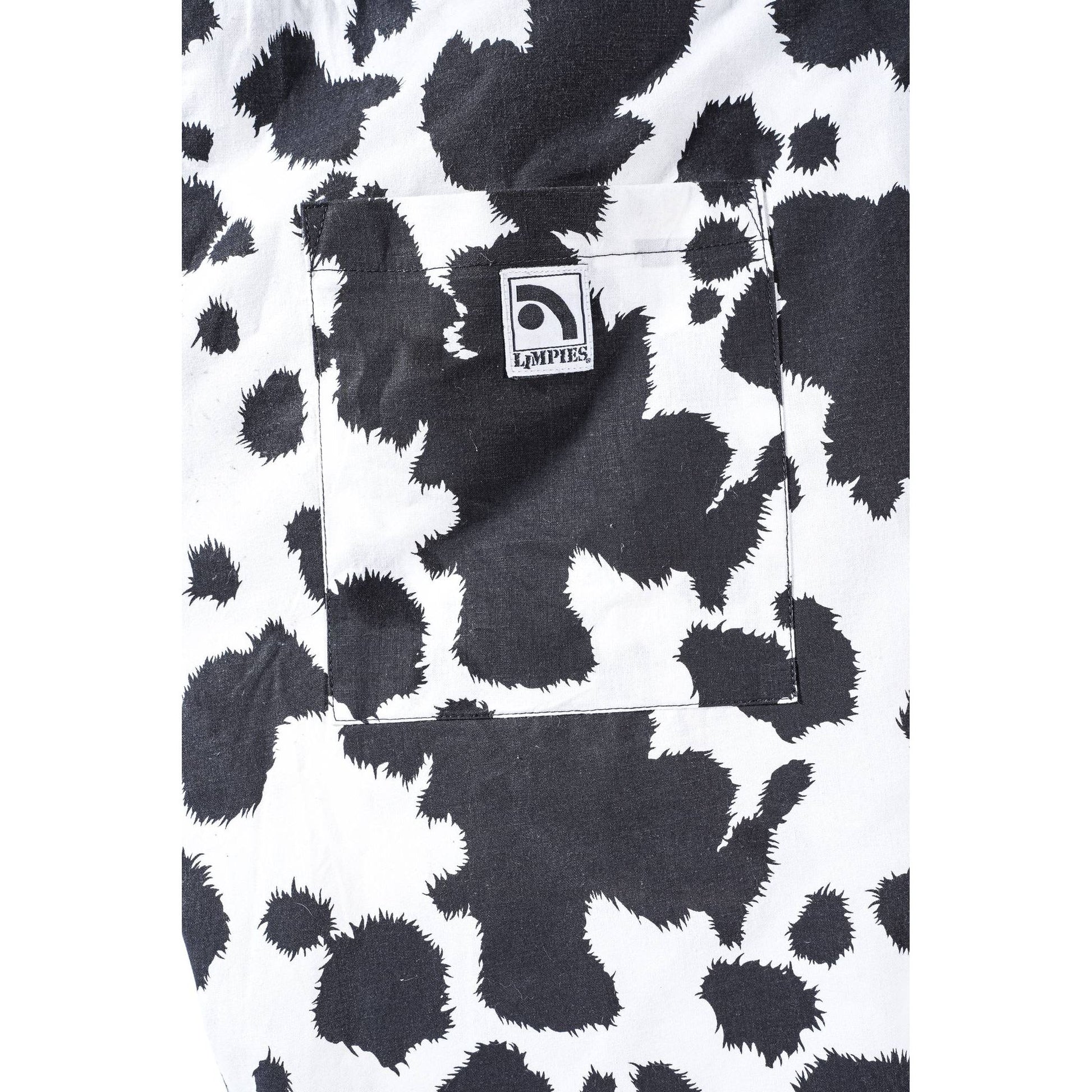 Close-up of a black and white cow-print  Limpies baggy skate short fabric garment, showing a front pocket with a square Limpies logo patch.