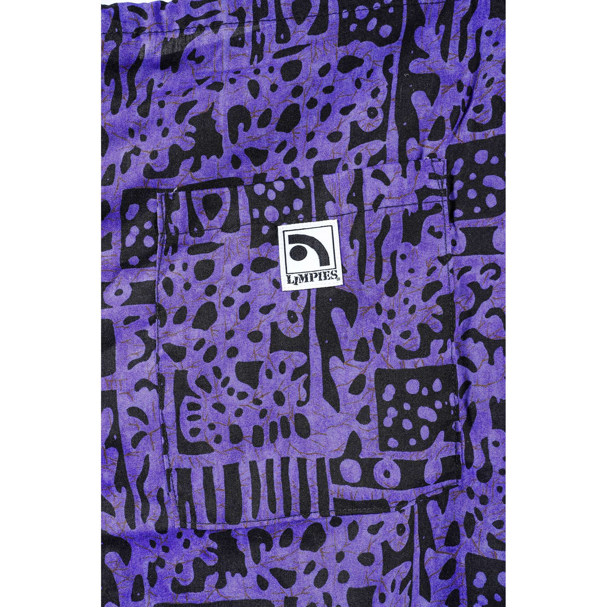 A close-up of a purple and black abstract patterned Limpies baggy skate shorts featuring a central white square patch with the brand name 'LIMPIES'.