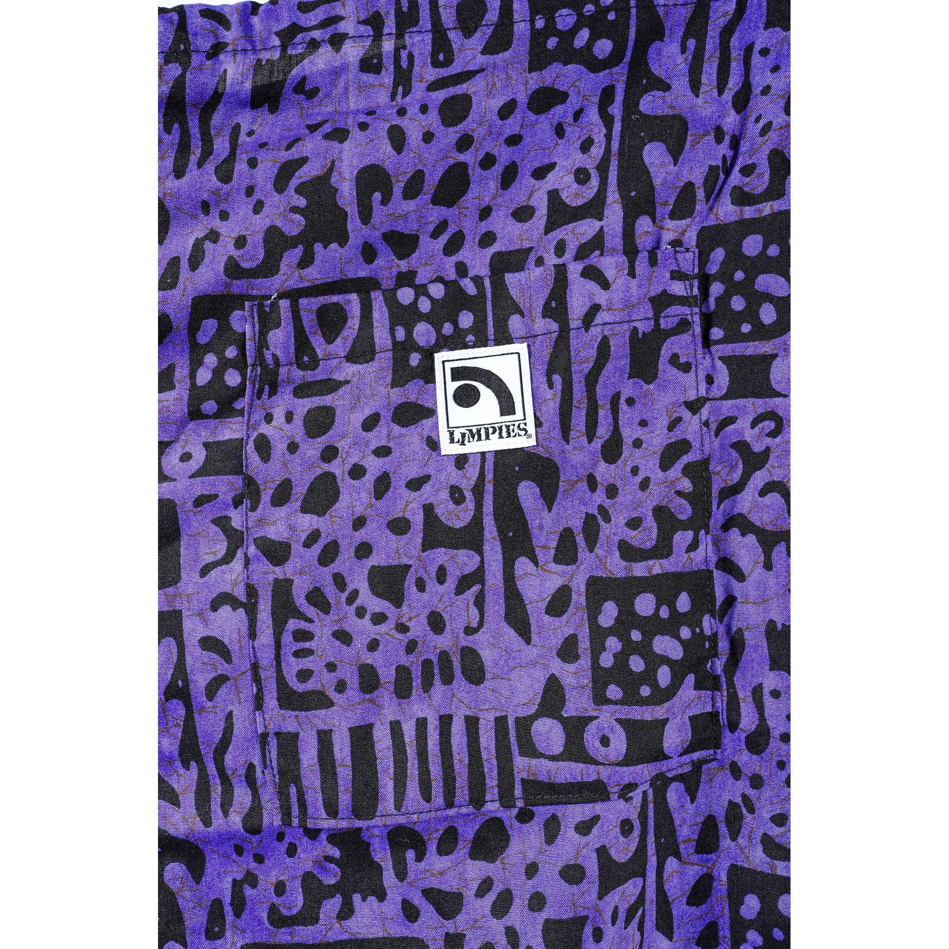 A close-up of a purple and black abstract patterned Limpies baggy skate shorts featuring a central white square patch with the brand name 'LIMPIES'.