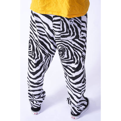 Black and white zebra spiral pattern baggy skate pants worn by a model, shown from the back with a yellow shirt and black sneakers visible.