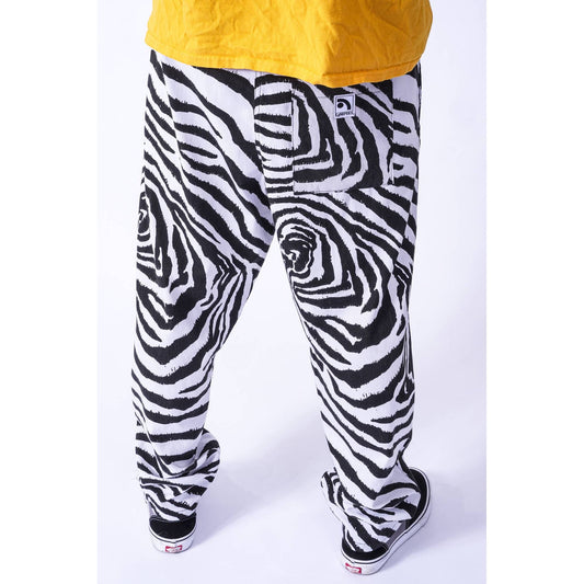 Black and white zebra spiral pattern baggy skate pants worn by a model, shown from the back with a yellow shirt and black sneakers visible.